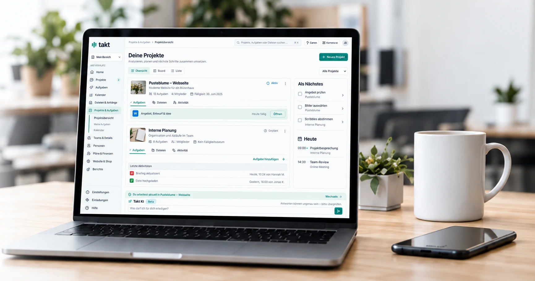 Heller Arbeitsplatz mit Laptop und Takt Projektübersicht, Smartphone und unbeschrifteter Tasse